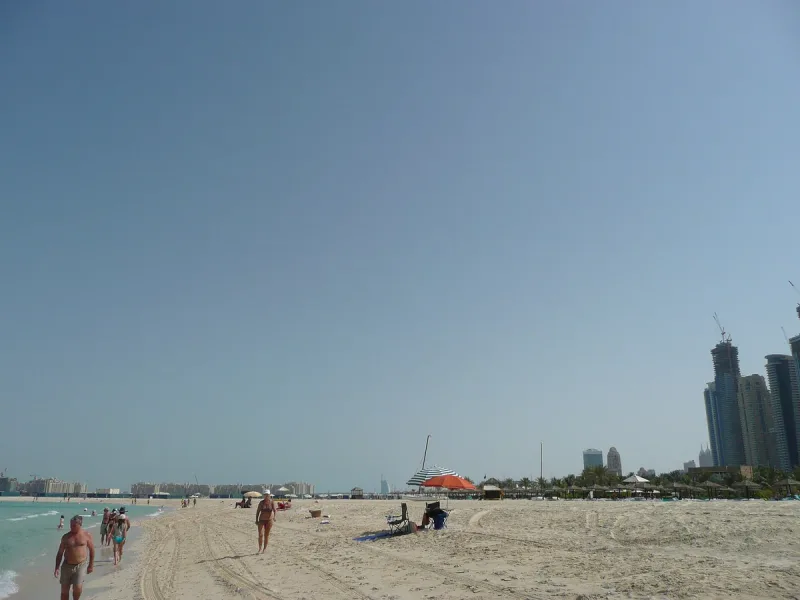 חוף חול רחב ורדוד, ובאופק מגדלים בהירים באובך