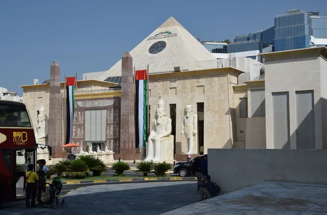 חזית בסגנון מצרי עתיק עם פסלים גדולים, עמודים ודגלים לצד גג משולש