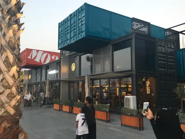 חנויות ובתי קפה במכולות ספנות כחולות ואדומות, עוברי אורח בחזית