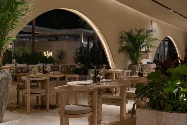פתחים מקושתים מוארים עם שולחנות עץ בהיר ערוכים וצמחייה בעציצים