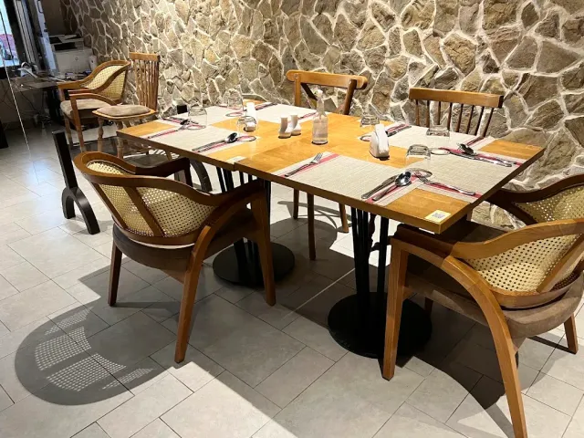 שולחן עץ ערוך עם כיסאות קש מול קיר אבן, על רצפת אריחים בהירה