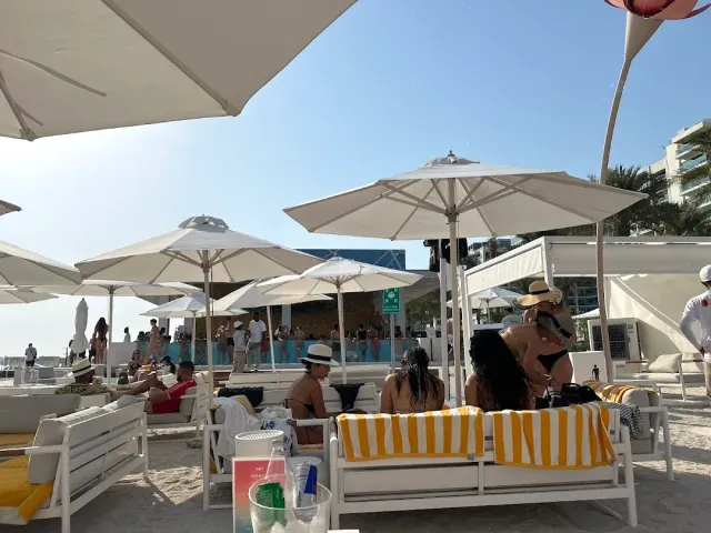 מיטות שיזוף עם מגבות פסים צהובות תחת שמשיות לבנות ליד בריכה