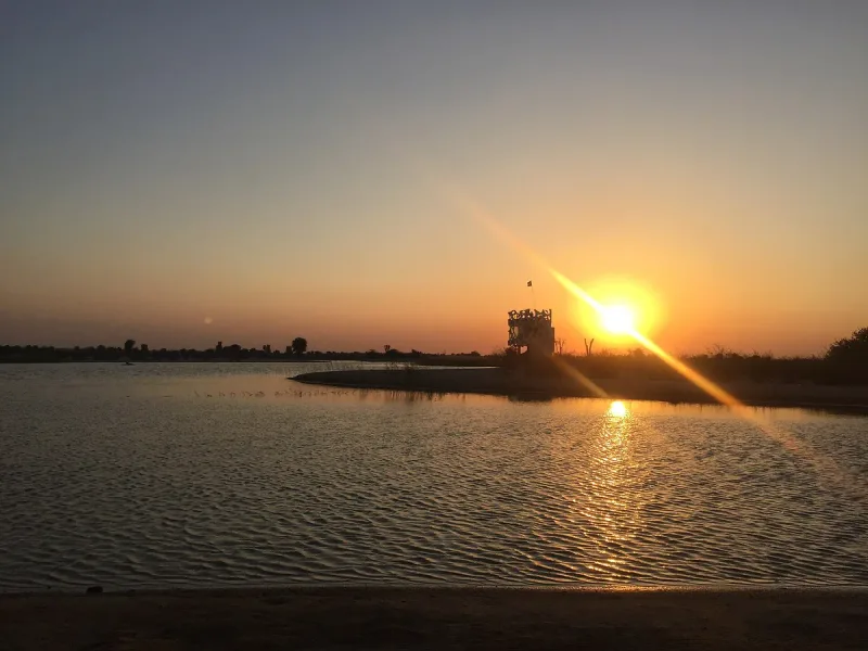 אגם מדברי רחב במים שקטים, השמש שוקעת מעבר לגדה ומשאירה שובל אור על המים
