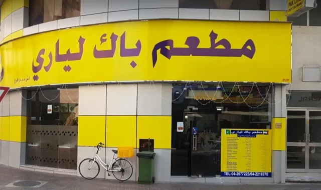 חזית פינתית צהובה עם שלט בערבית, אופניים לבנים ותפריט תלוי על הקיר