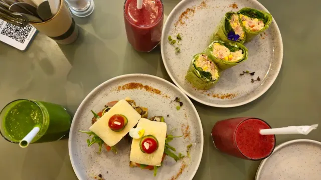 מבט מלמעלה על צלחות כריכים ולפיתות לצד שייק ירוק ושני משקאות אדומים
