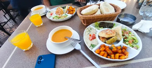 שולחן חוץ עם קערת מרק כתום, מגש מזה, סלסלת לחם וכוסות מיץ