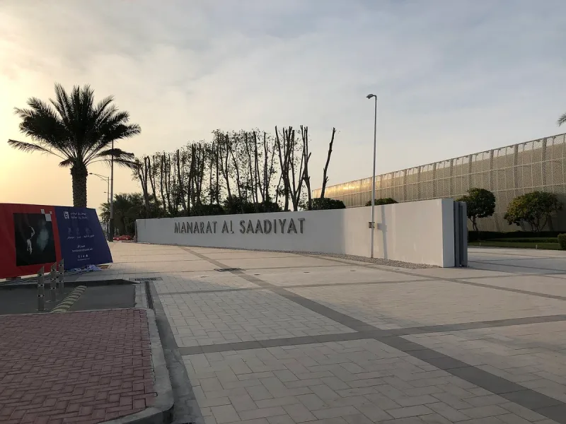 קיר הכניסה שנושא את השם מנארת אל סעדיאת, ומאחוריו חזית המתכת המחוררת של מרכז האמנות, בשעת בין ערביים