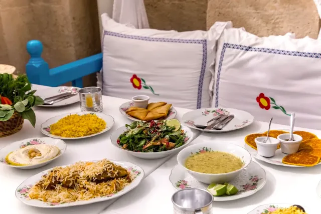 שולחן לבן ערוך במנות אורז, חומוס וסלט, מול כריות רקומות בפרחים אדומים
