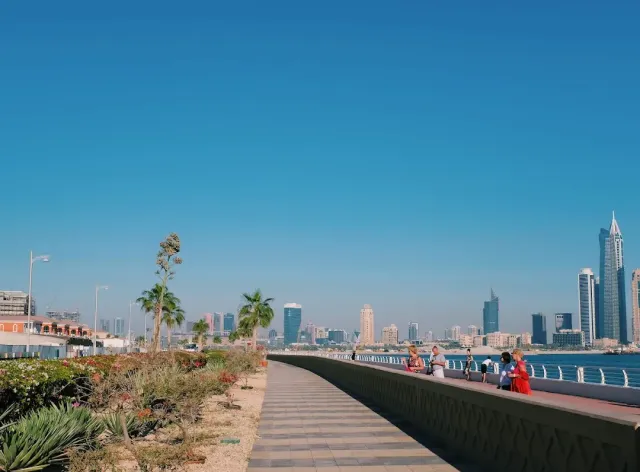 טיילת מרוצפת לאורך חומת ים, עם צמחייה נמוכה וקו רקיע ברקע