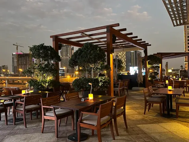 מרפסת גג בשעת דמדומים עם פרגולות עץ, שולחנות עם נרות וקו רקיע מואר