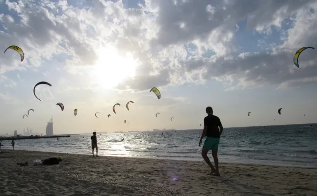 עשרות עפיפוני גלישה בשמים מעל הים ואדם הולך על החול