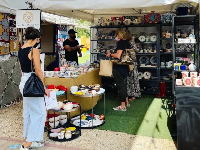 דוכן שוק מקורה עם כלי חרס וקערות צבעוניות, וקונות מתבוננות בסחורה